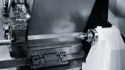 Metal rod spins precisely between lathe chuck jaws. Fine metal shavings fly from the cutting tool. Industrial precision manufacturing environment. Mechanical engineering process captured in detail © Aleksandr Matveev
