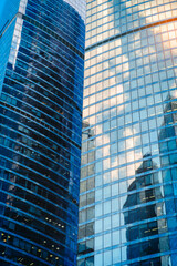 Fototapeta premium Tall glass skyscrapers of business offices in city reflect blue sky, clouds, and other skyscrapers. Sunlight glistens on glass surface. modern cityscape of city's business district. 