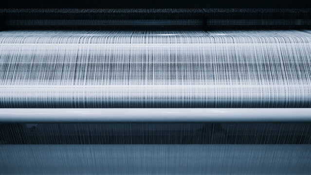 Close-up of a textile weaving machine in operation. Fabric threads move through the machine's rollers smoothly.  woven material has light, textured appearance