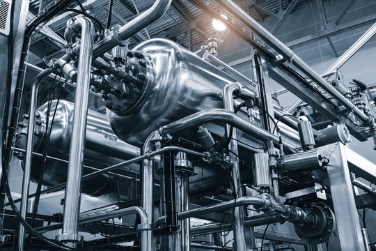Industrial piping system in monochrome. Stainless steel pipes form complex network. Visible valves and connections in factory setting. Clean technical photography