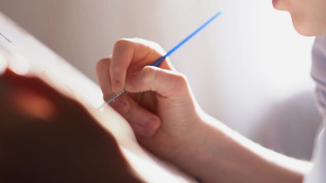 A teenager paints a paint-by-numbers picture on canvas with a brush. A boy dips a brush into paint and creates a creative drawing on a canvas. High quality FullHD footage