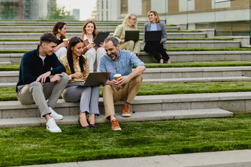 Fototapeta premium Colleagues collaborating outdoors on laptop during casual business meeting on stepped lawn