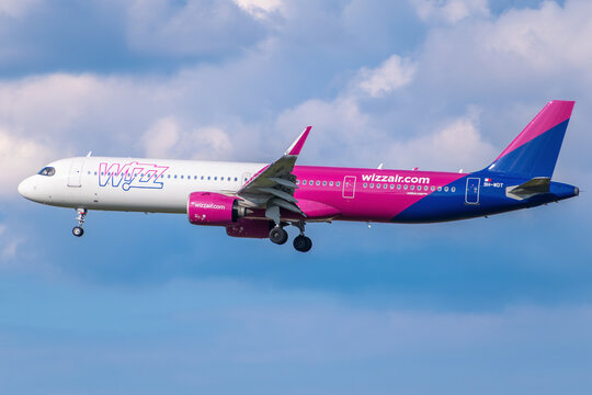 Wizz Air Airbus A321neo passenger jet, registration 9H-WDT, descending for landing against a cloudy blue sky.