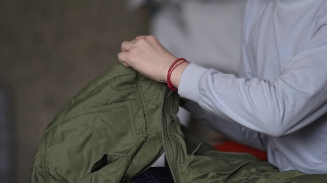 A teenager is busy sorting through and putting away winter clothes, closing the zipper on a down jacket to put them away in vacuum bags. High quality FullHD footage