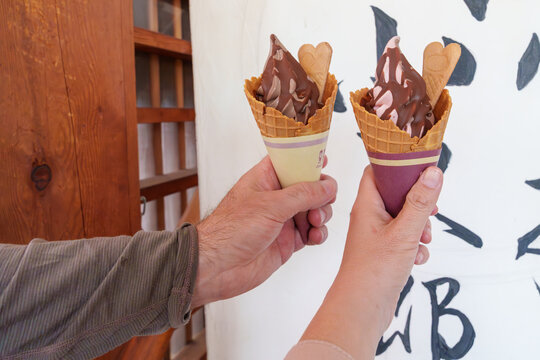 Two hands hold up soft serve milk ice cream waffle cones with chocolate