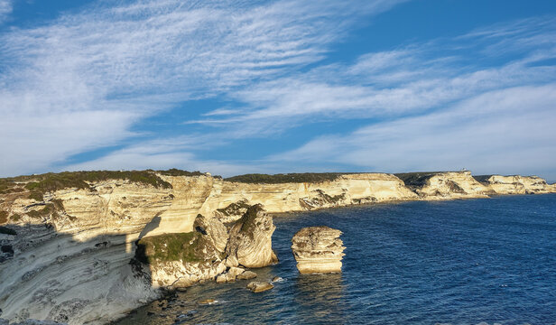 Breathtaking view of the famous white limestone cliffs of Bonifacio and the Grain de Sable sea stack under a blue sky. Beautiful coastal landscape of southern Corsica island, France. 