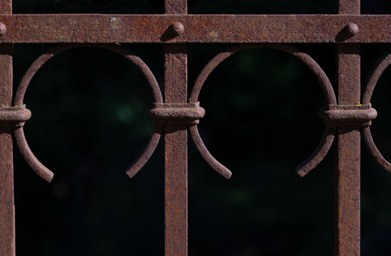 A close-up of an old, rusty metal fence. The background is dark.