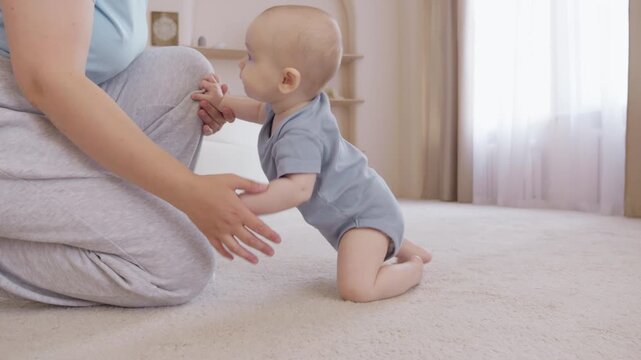 Caucasian baby crawling across carpet reaching for mothers hands to be pulled up, intimate nursery scene, curious exploration and early standing practice with gentle