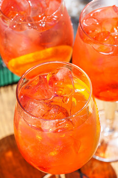 Close up glasses of refreshing orange spritz cocktails with ice and citrus slices served outdoors on green sunny patio. Summer relaxation, outdoor dining, leisure, travel and social gathering concept.