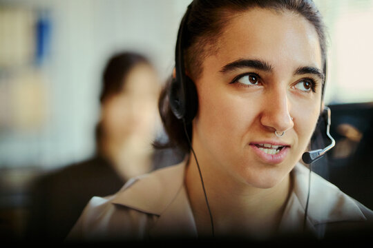 Close up of young adult woman wearing headset, assisting customers in call center office and supporting service operations. Ideal for customer support, CRM, contact us marketing