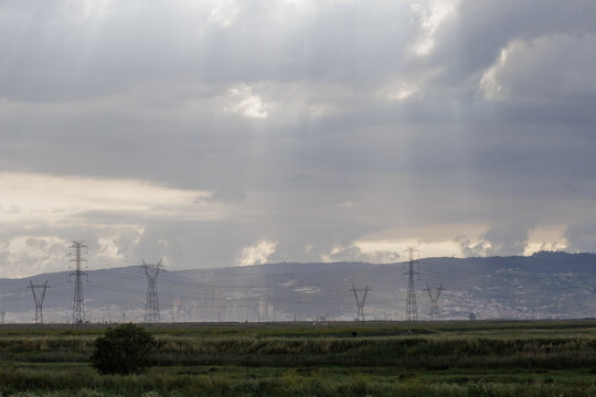 Transmission towers crossing green landscape under sunrays breaking through clouds