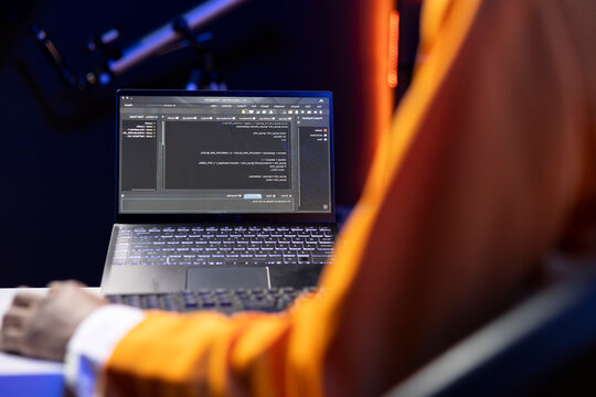 Person in home office looking at UI on laptop screen, typing and executing programming code; coding application UI used by IT developer writing and testing code in modern workspace, close-up shot.