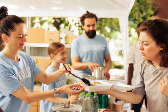At an outdoor food bank, caucasian family volunteering a variety of food items to assist the hungry and less fortunate individuals; nonprofit group supports hunger relief by serving nutritious meals.
