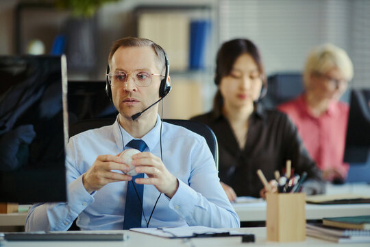 Medium shot of Caucasian middle aged man wearing headset, working at call center desk with team in office. Illustrating customer support, sales service, professional business staffing