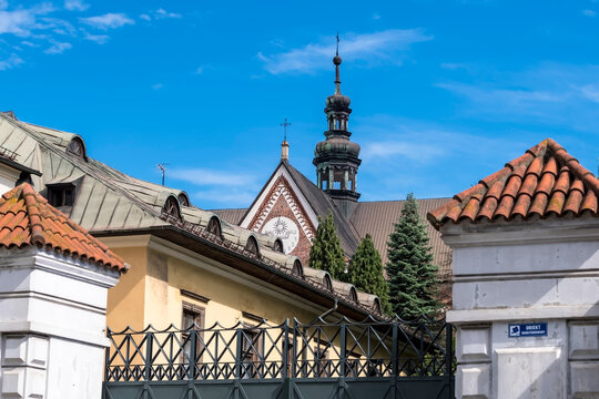 Piękny, zabytkowy, średniowieczny kości&oacute;ł i klasztor cysters&oacute;w w Krakowie w słoneczny, wiosenny dzień. Na zdjęciu widać fasadę zegarową z misternymi wzorami z cegły Z dachu wznosi się iglica z krzyżem