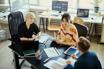 Fototapeta premium Diverse business team collaborating in office, reviewing reports and discussing strategy during meeting. Ideal for workplace teamwork, project management, corporate planning concepts