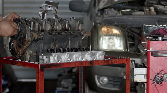 Close up shot of auto mechanic hands fixing a disassembled vehicle engine block on a workbench in car repair service garage. Cylinder head and tools visible in background. Cinematic footage.