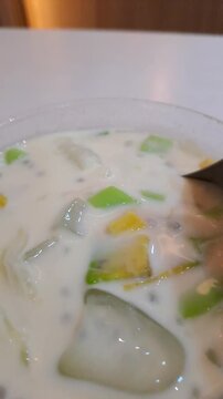 Close-up of an Asian woman enjoying a viral creamy Durian Es Teler in a cafe. The footage captures her stirring the refreshing Indonesian iced dessert filled with avocado, coconut, jackfruit, and prem