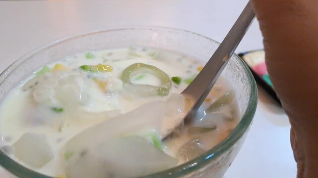 Close-up of an Asian woman enjoying a viral creamy Durian Es Teler in a cafe. The footage captures her stirring the refreshing Indonesian iced dessert filled with avocado, coconut, jackfruit, and prem