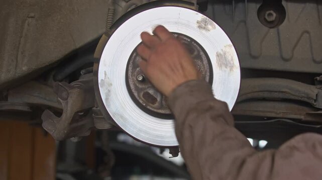 Close up shot of auto mechanic hands replacing a shiny new brake disc rotor on a vehicle hub assembly in car repair service garage workshop. Cinematic professional maintenance footage.