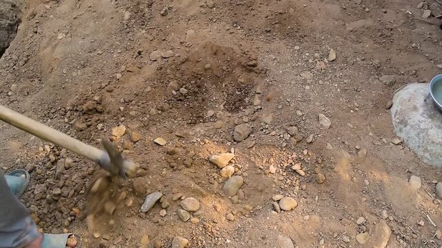 Closeup of man's hands digging rocky soil with a pickaxe tool on the ground manual labor and excavation