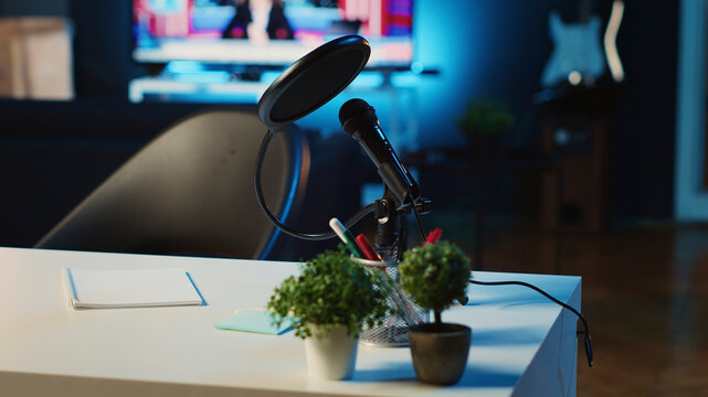 Coffee table with microphone and mini house plants in dimly lit empty home studio interior. Podcast recording equipment in apartment illuminated by RGB lights, close up.