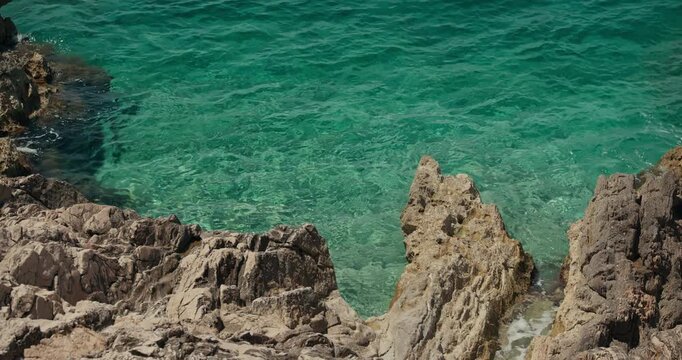 Crystal clear Adriatic water surrounds rugged coastal rocks along the shore in Primosten, Croatia.