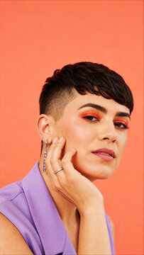 Portrait of stylish individual with short pixie undercut and bold orange makeup on solid orange background.