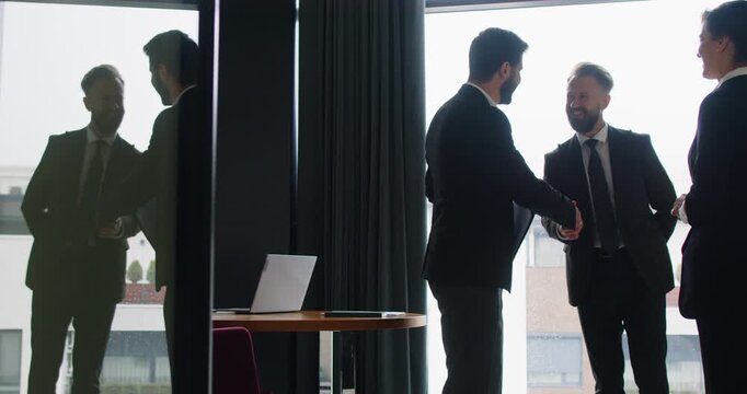 Business successful team meeting celebrating in modern office after negotiating on project, investment, discussing work issues, contemporary interior with glass wall, big panoramic window, reflection