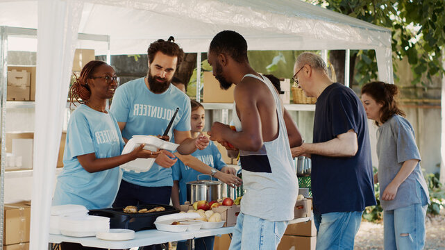 Humanitarian aid team graciously providing free warm meals to the poor needy and less fortunate individuals, group of volunteers handing out food donations to the homeless people.