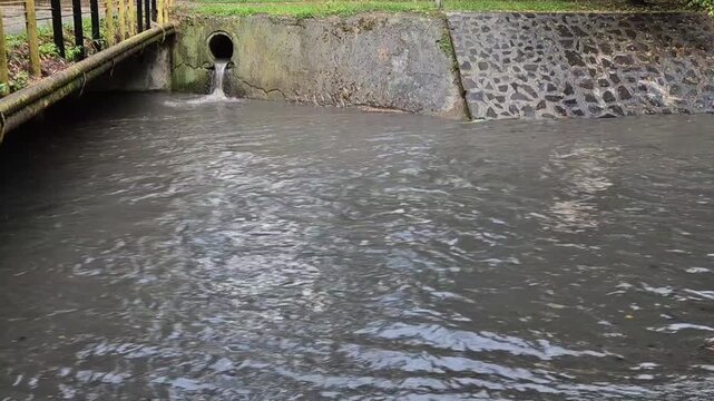 Storm Drain Pipe Discharging Water Into Urban Canal During Heavy Rain