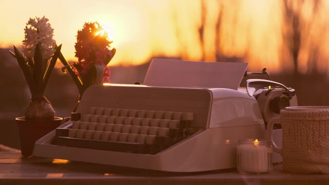 Vintage typewriter with blank paper on table sunset, lit candle, inspiration artistic journaling process, warm golden light, creative writing concept, nostalgic atmosphere, blurred nature background