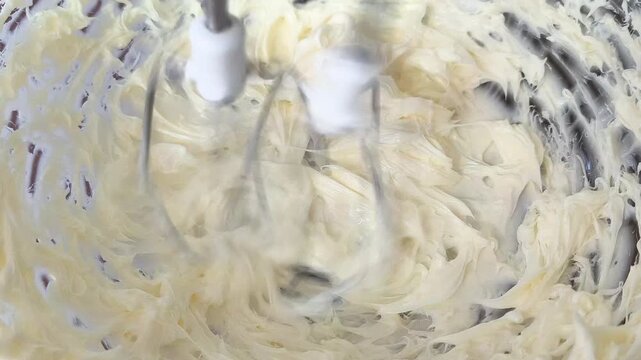 Electric mixer whips smooth buttercream frosting into a light fluffy texture creating creamy dessert filling for cake decorating baking and pastry preparation