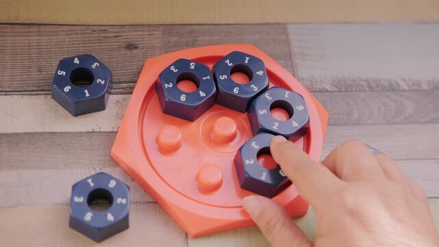 Hand placing numbered blue hexagonal puzzle pieces orange educational game board, developing logic and math skills, STEM toy, mental exercise, cognitive development, problem solving, matching numbers