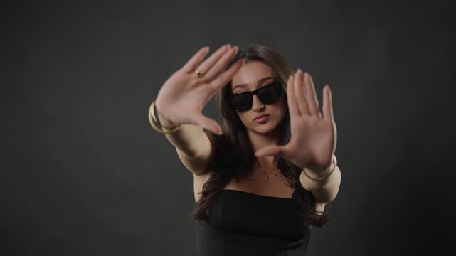 Female model posing confidently in sunglasses, embodying beauty and fashion concepts. This studio shot with a dark background highlights her stylish eyewear and elegant demeanor. The young woman s exp