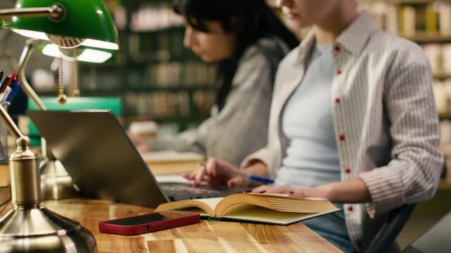 Student writing on textbook and loses focus after receiving phone notification, leaving coursework unfinished while scrolling on smartphone beside laptop.