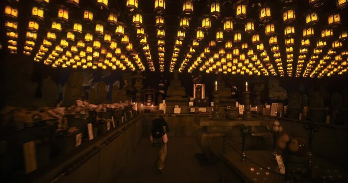 Young Visitor Walks Through Ancient, Lantern-Filled Buddhist Temple Hall In Japan - Steady Cam