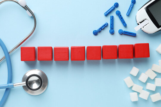 Diabetes control. Empty wooden cubes, stethoscope, sugar cubes, lancets and digital glucometer on light blue background, flat lay