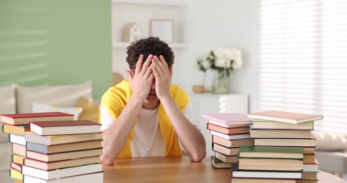 Teenage boy with many books at wooden table indoors