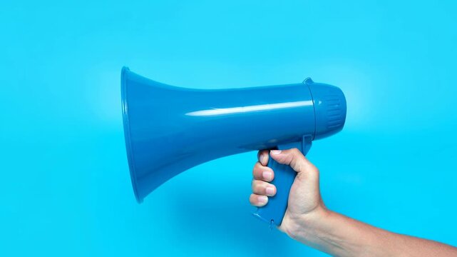 Hand holding blue megaphone on bright blue background for announcement and communication concept