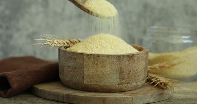 Woman putting semolina into bowl at wooden table, closeup