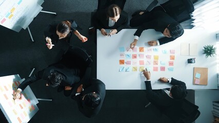 Naklejka premium Top down aerial view of business group sharing and brainstorming idea by using sticky notes at meeting room. Investor writing marketing strategy on board while receive note from manager. Directorate.