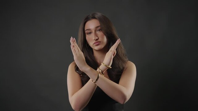 Rejection and disapproval concept, a young woman making a stop gesture with crossed arms. This negative emotion, boundary setting, and refusal. The studio shot with a dark background emphasizes her se
