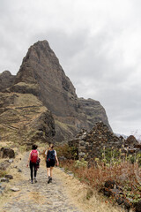 Obraz premium Two Hikers on Rocky Trail with Volcanic Peak Santo Antao