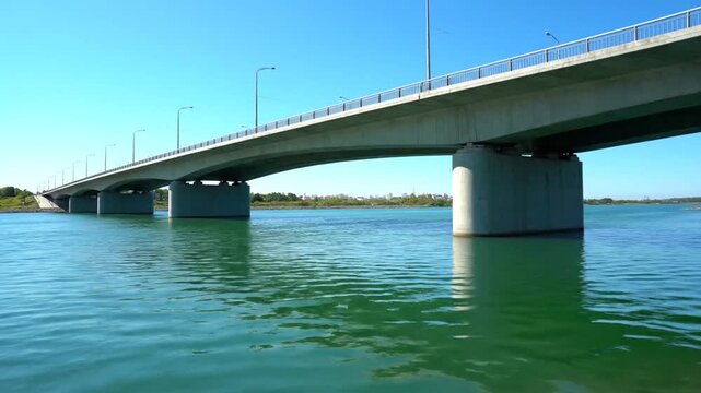 A long concrete bridge spans across a calm blue river water