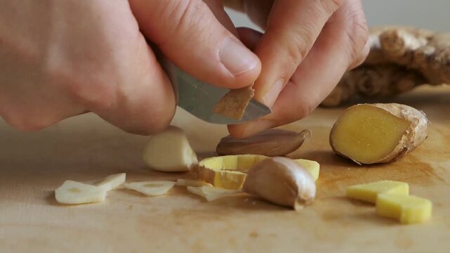 person peeling ginger sliced ginger and garlic on cutting board picking up the pieces close up.