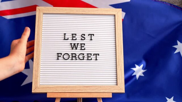 Somber Australian flag backdrop with text LEST WE FORGET on letter board. Respectful message for memorial ANZAC campaigns. Concept of remembrance and honor