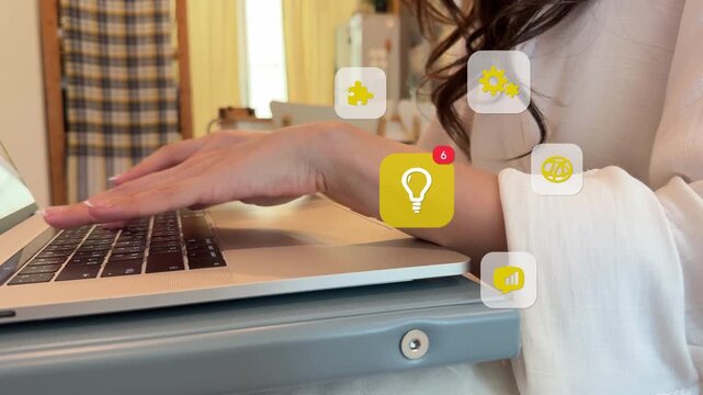 Side profile close up of a young East Asian woman typing on a laptop computer, with virtual lightbulb, globe, gears, and puzzle piece graphics popping up around her hands.