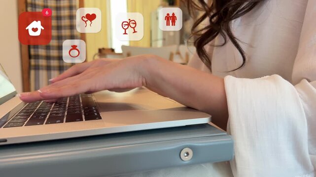 Close up of an East Asian woman using a laptop to organize a wedding event, with virtual house with heart, diamond ring, wine glass, and bride groom couple icons popping up.