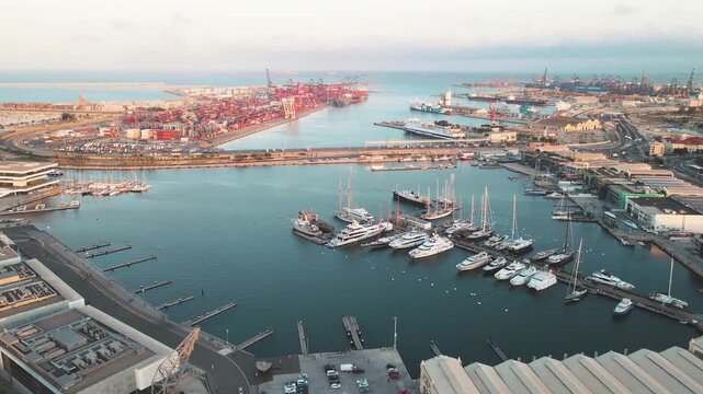 Aerial harbor view shows boats, yachts, and cargo ships. Port facilities and city skyline are visible. Busy marina activity captured. Marina docks hold numerous boats and yachts